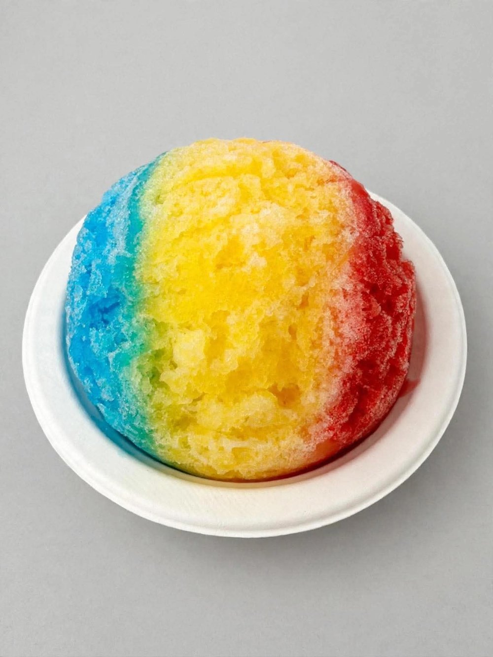 Rainbow shave ice with blue, yellow and red syrup on a plate